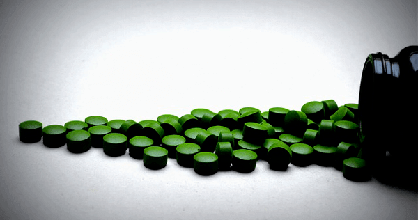 Sun Chlorella tablets appear to have been spilled out of a bottle onto a hard surface