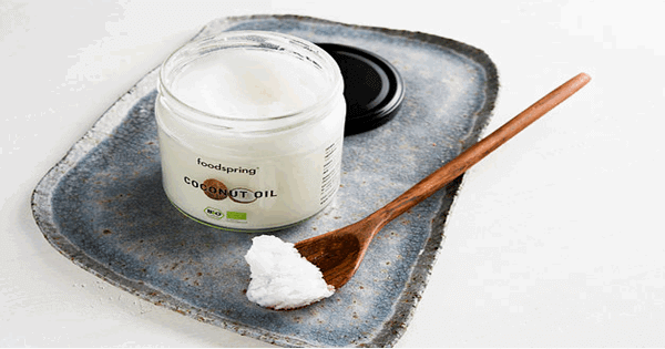 jar of coconut oil along with a wooden spoon full of it, both sitting on a tray