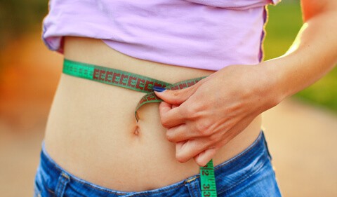 a closeup view of a female's mid-section showing her holding a measuring tape around her waist